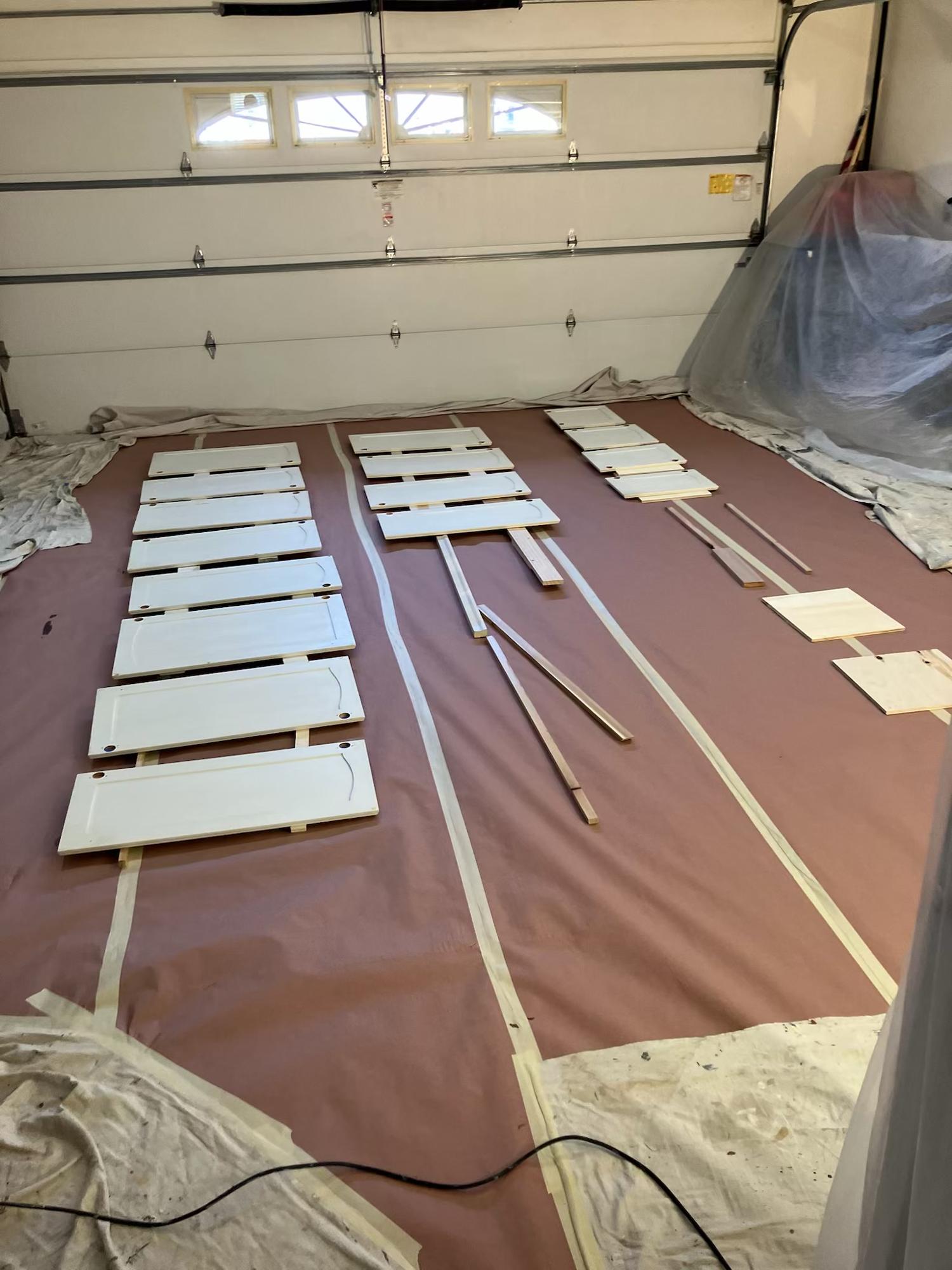 Cabinet doors laid out in rows on protective paper in a garage