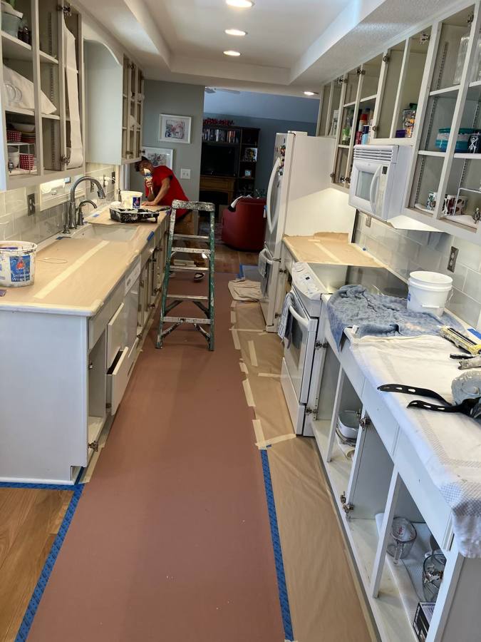 Galley kitchen with floors and counters covered in protective paper and blue tape