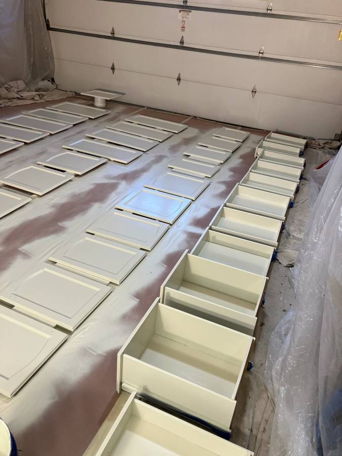 Freshly painted white cabinet doors and drawers laid out in rows to cure