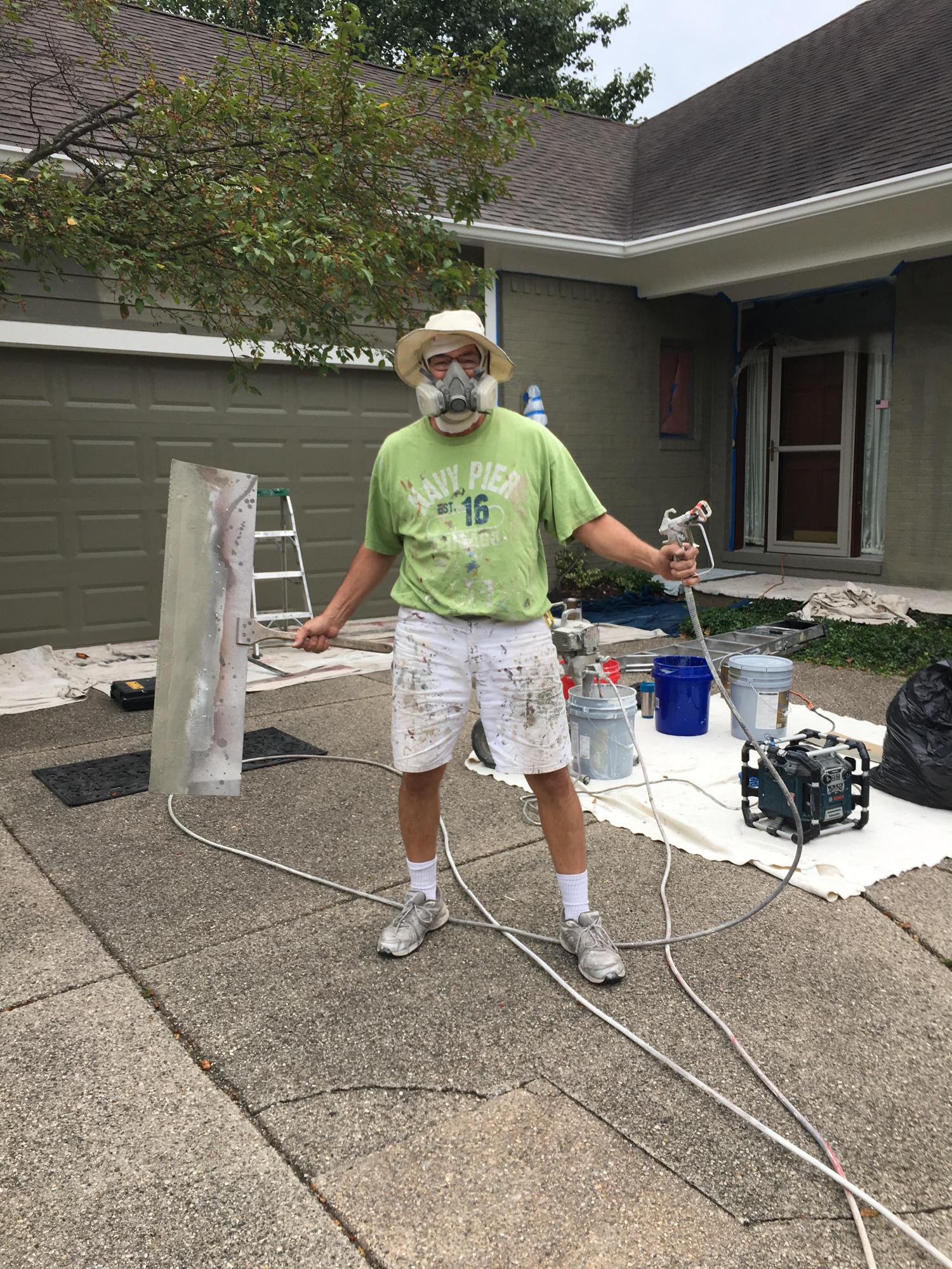 Dan on a driveway using a paint sprayer with protective gear