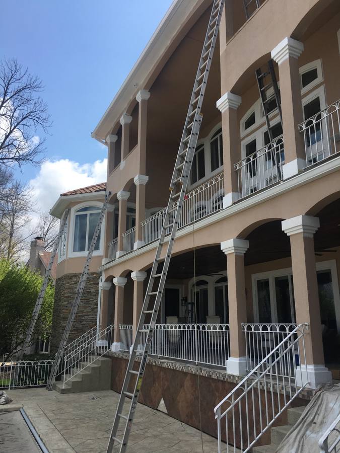 Tall extension ladders set against a three-story stucco home with balconies