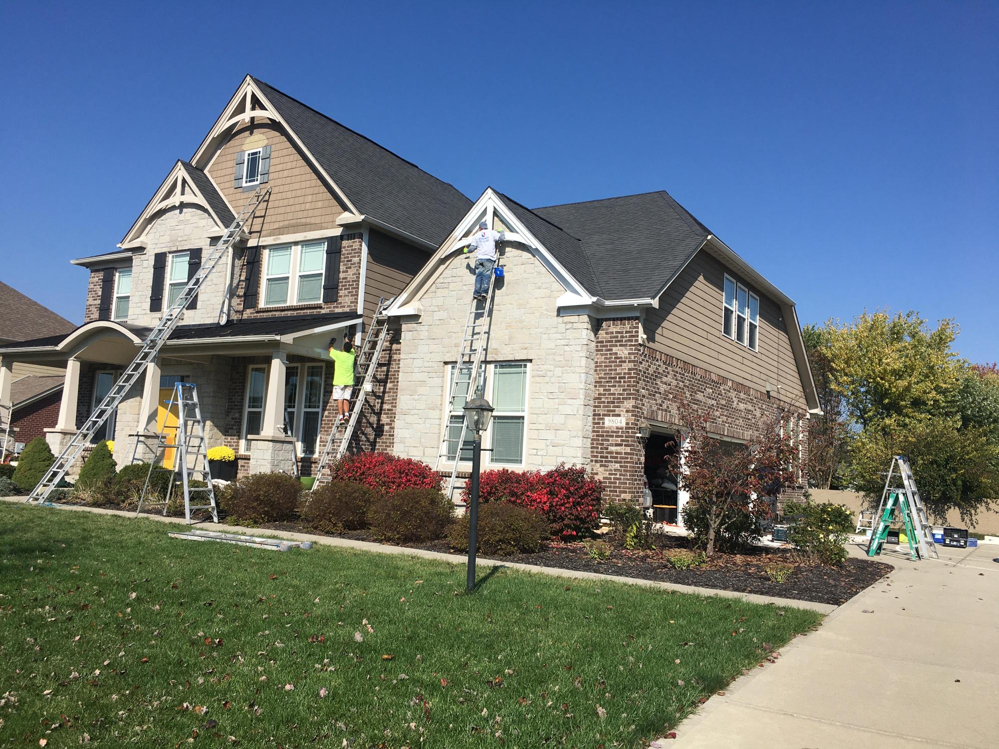Crew on ladders painting the exterior of a stone and siding home